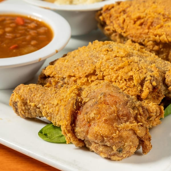 Crispy fried chicken pieces and a bowl of baked beans on a white plate at Felix's BBQ with Soul.
