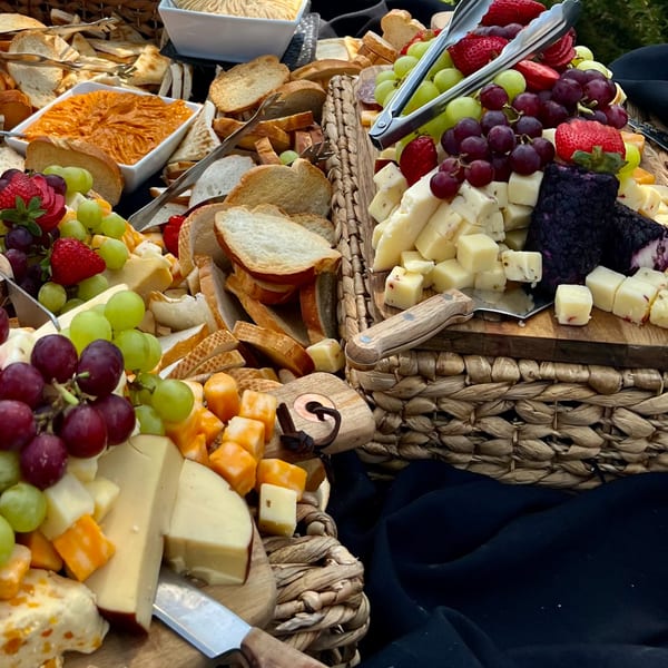 A lavish charcuterie spread with cheeses, grapes, strawberries, crackers, and dips on woven baskets.