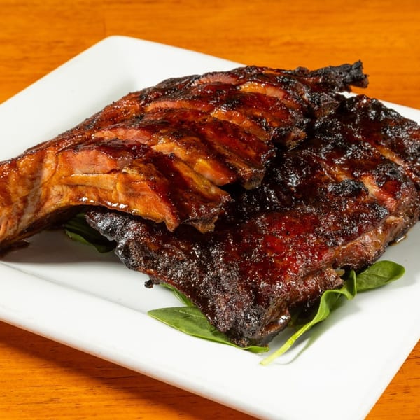 Felix's BBQ with Soul's glistening, dark brown ribs on a white plate with green garnish.