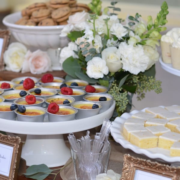 Dessert table with crème brûlée, lemon bars, chocolate chip cookies, and white floral arrangements.