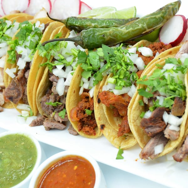 A plate of various tacos with cilantro, onions, grilled peppers, radishes, and two bowls of salsa.